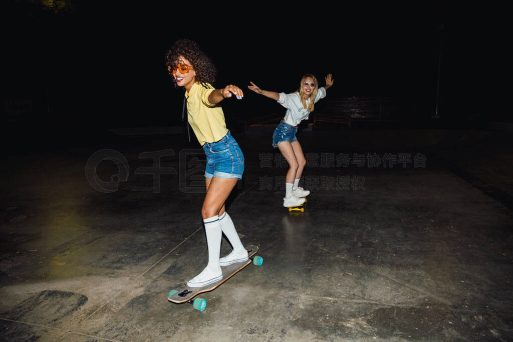 Image of two multinational girls smiling and riding skateboards