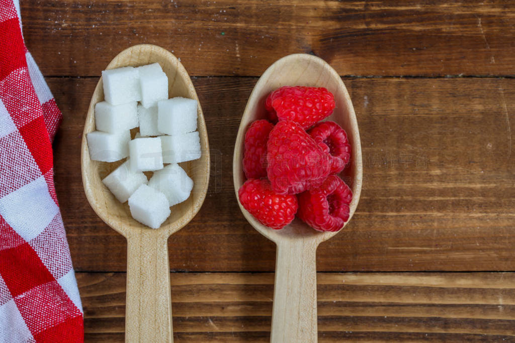 Healthy raspberries and unhealthy sugar in wooden spoons