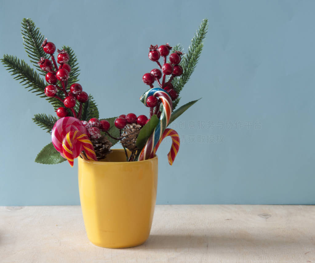 Christmas candy canes in yellow mug with berries holly branches