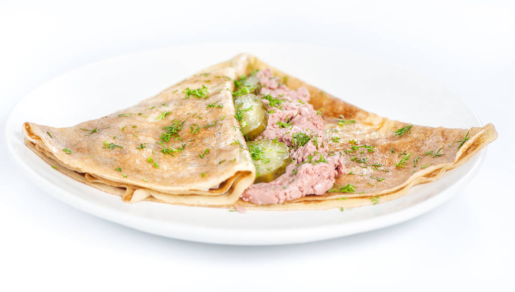 Thin delicious pancake with meat pate and cucumber on white