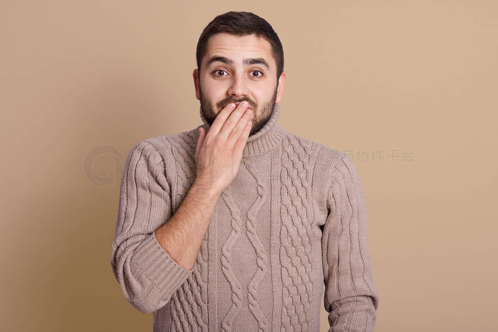 Emotive positive young male covering mouth, trying to stop laugh