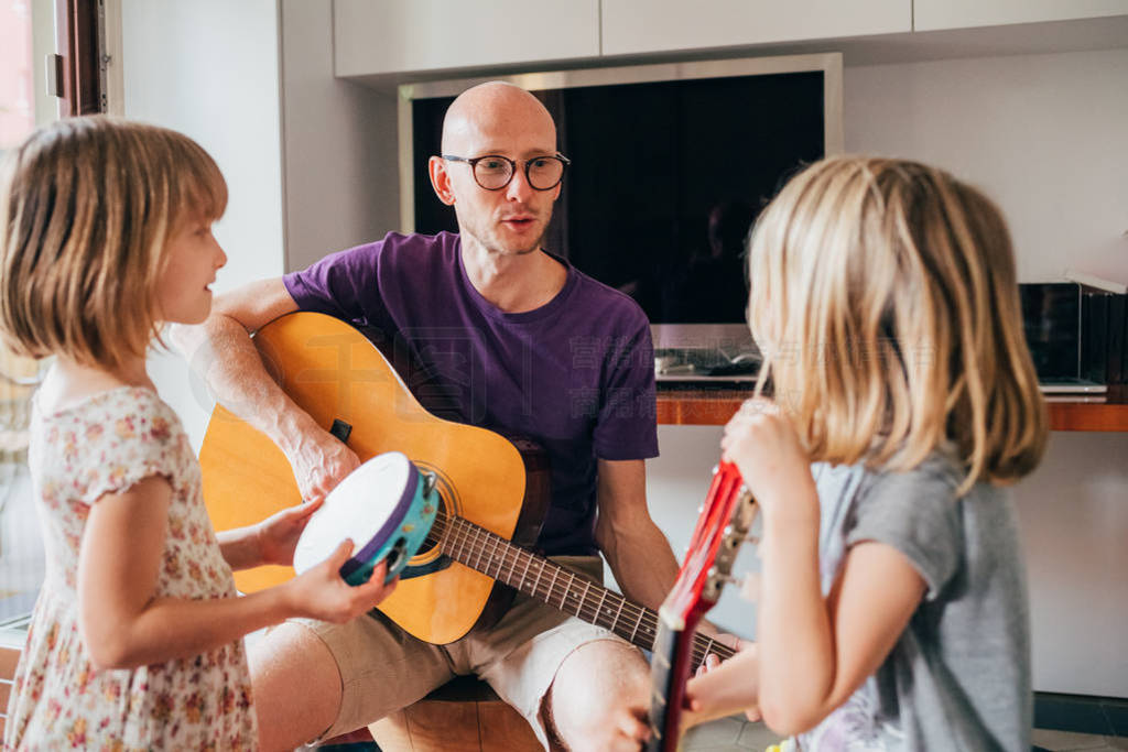 father teaching to his daughters how to play guitar and playing
