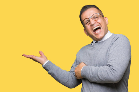 中年商务英语阿拉伯男子戴着眼镜，背景偏僻，用手和张开的手掌指向一边，呈现出微笑、快乐和自信的广告
