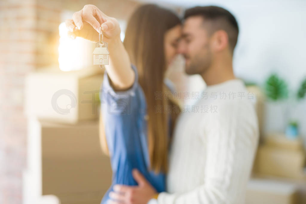 Young couple moving to a new home, hugging in love showing keys