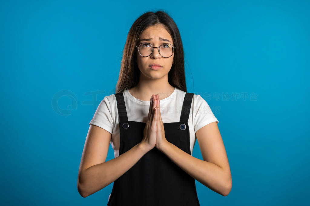 Cute asian young girl praying over blue background. Woman in gla
