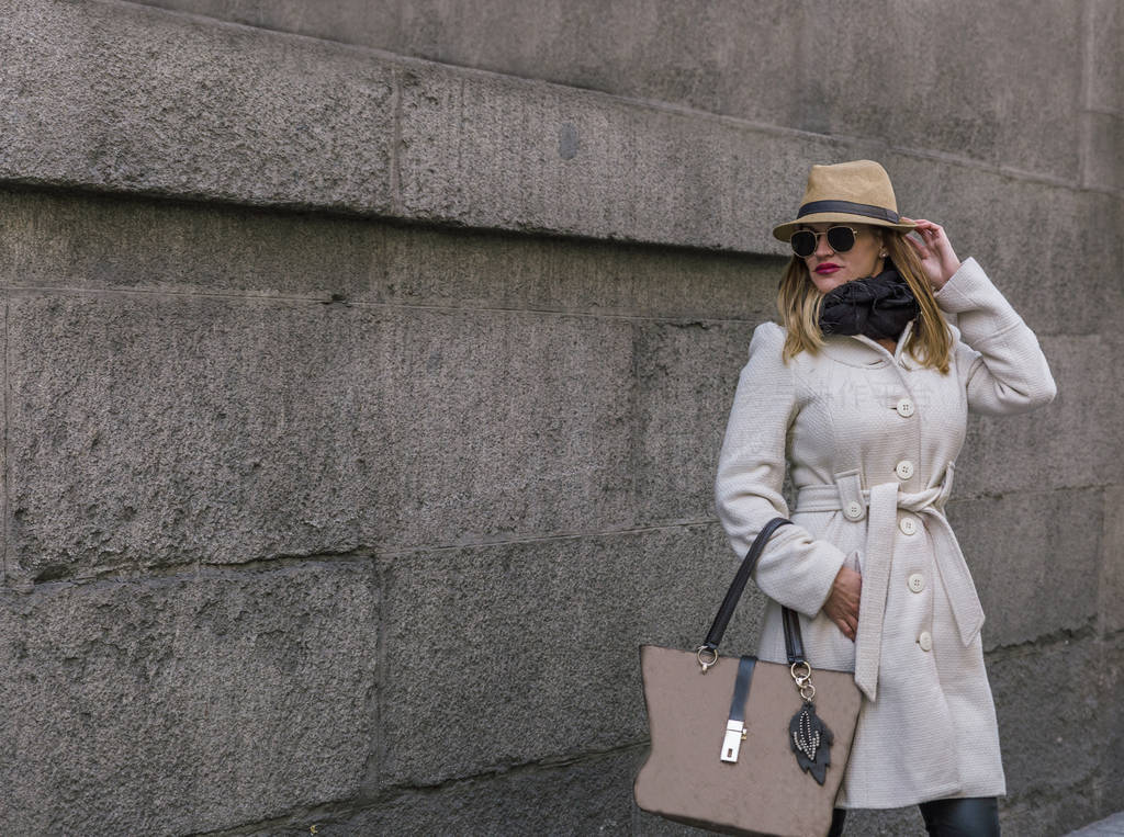 Elegant blonde woman with black glasses coat and hat walks down