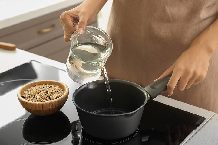 女人倒水,在爐子裡的平底鍋裡準備米飯