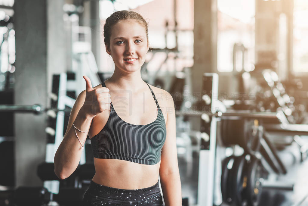 Healthy woman showing thumb up sign in fitness gym