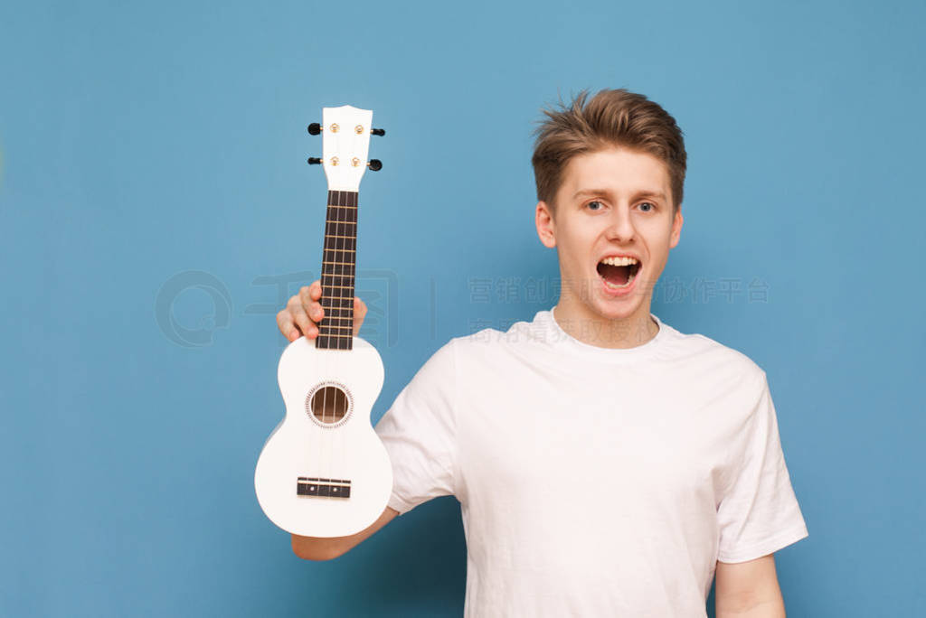 Emotional guy in a white T-shirt holds a ukulele in his hands, l