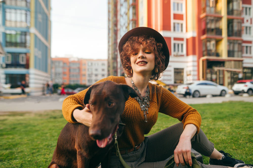 Portrait of happy girl sitting on lawn with dog, stroking puppy