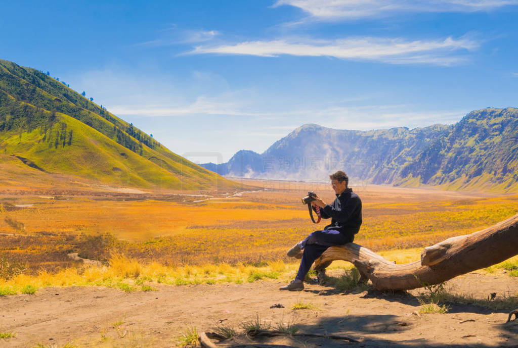 An Asian man, a photographer, holding a camera at Bromo Savanna