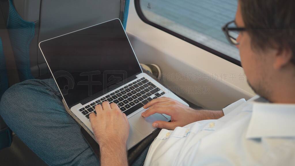 Young businessman with dark hair using his laptop while riding a