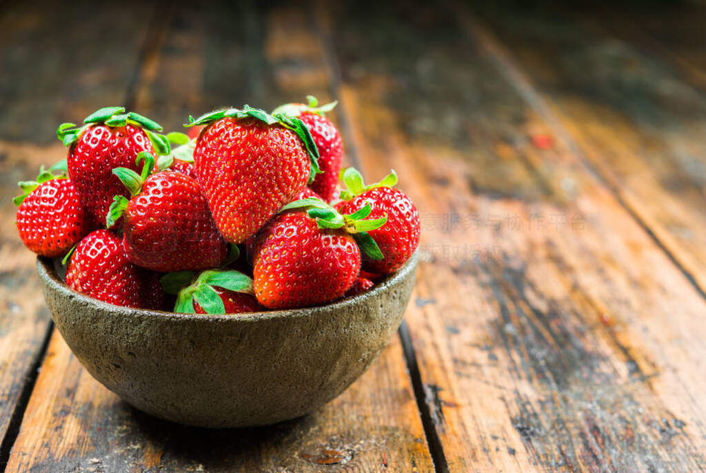 Bowl with fresh colorful organic strawberries fruit against wood