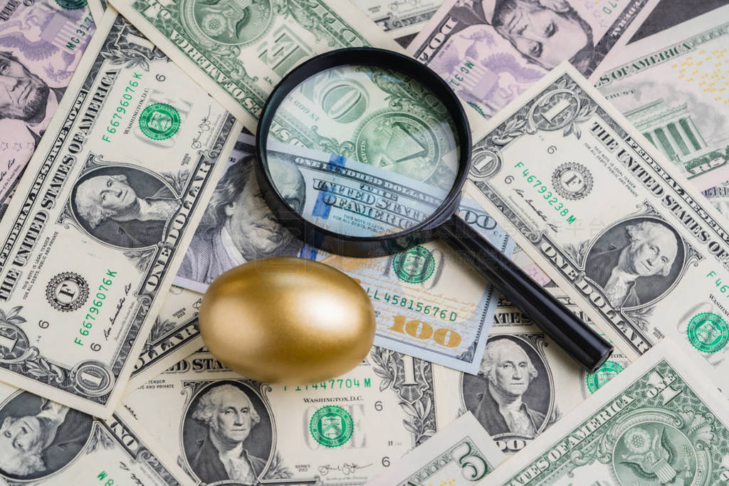 Magnifying glass with shiny golden egg under pile of US America