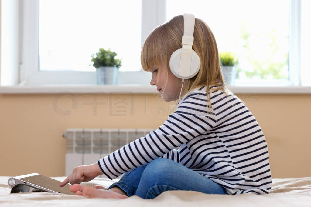 Little blond girl streaming online on tablet with headset.