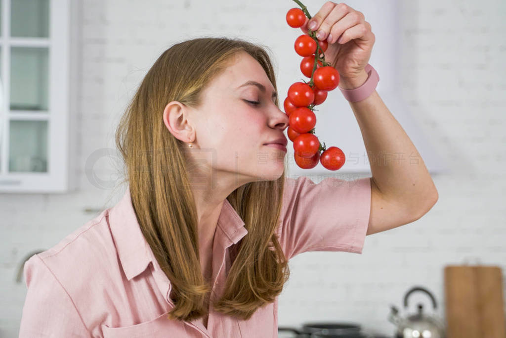 Girl in a pink dress sniffs a sprig of red cherry tomato.