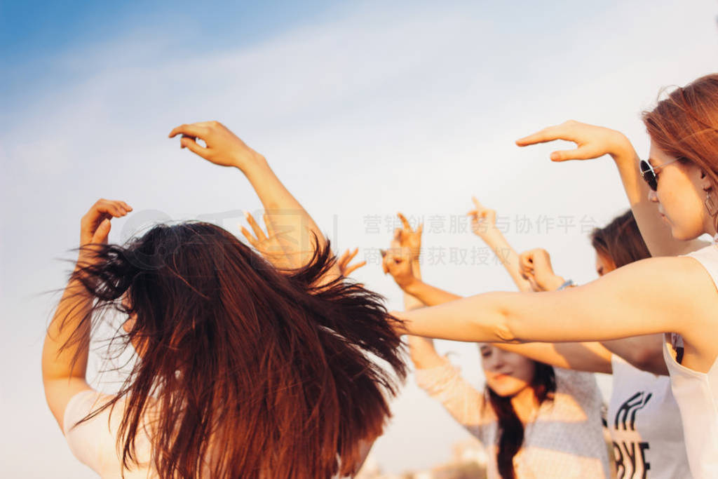 Group of young happy dancing tan girls on blue sky background, s