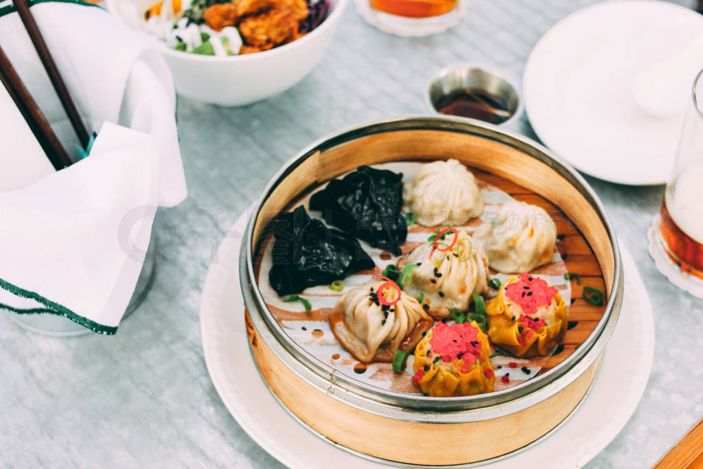Pan-Asian food - different dim sums in a bamboo bowl and salad