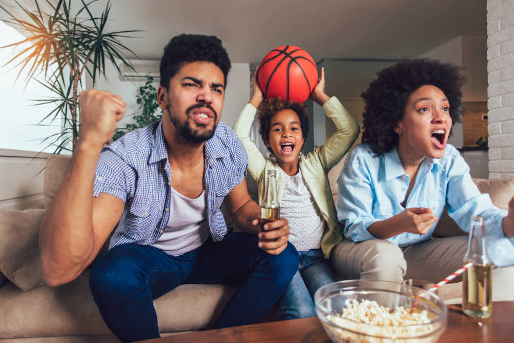 Happy African American family of three watching tv and cheering