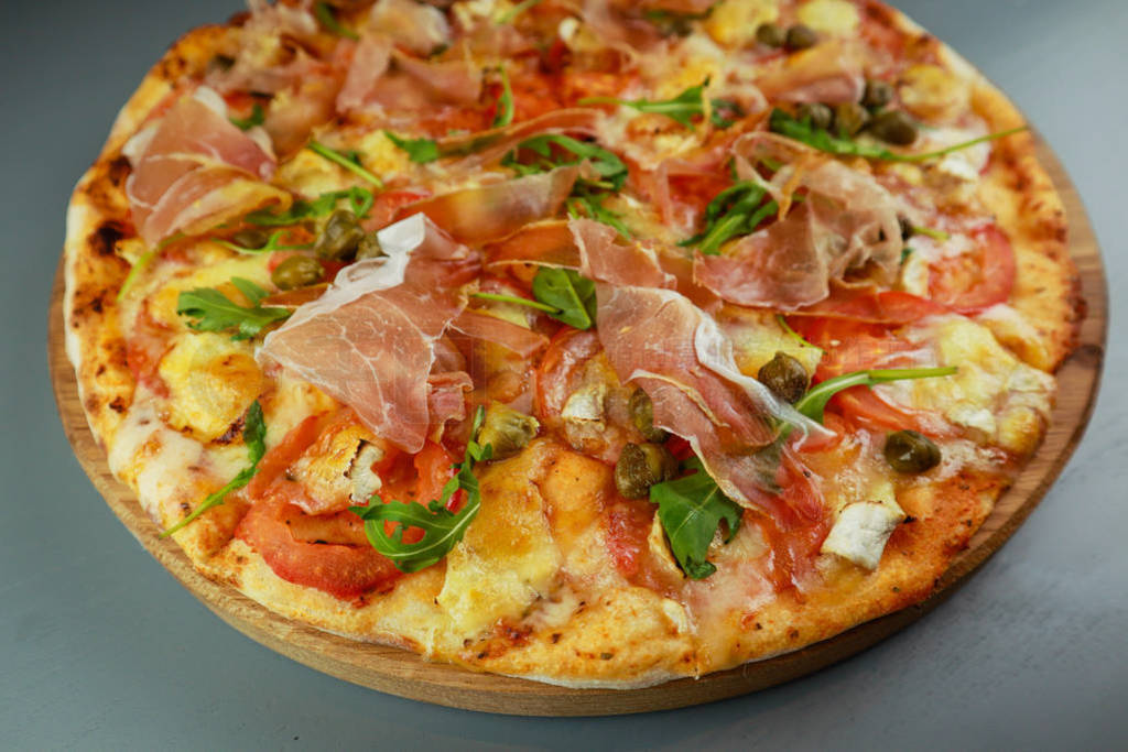 The pizza is prosciutto. Capers, tomatoes, arugula, mozzarella,