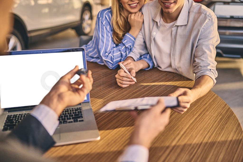 Handsome man and cheerful girl buying a car in showroom.