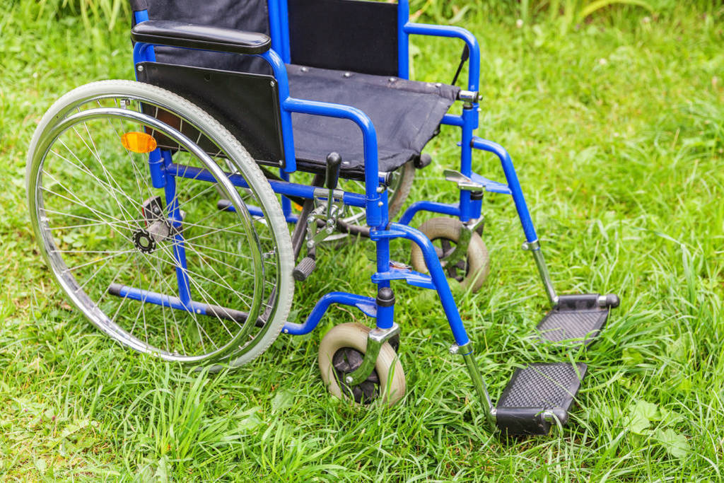 Empty wheelchair standing on grass in hospital park waiting for