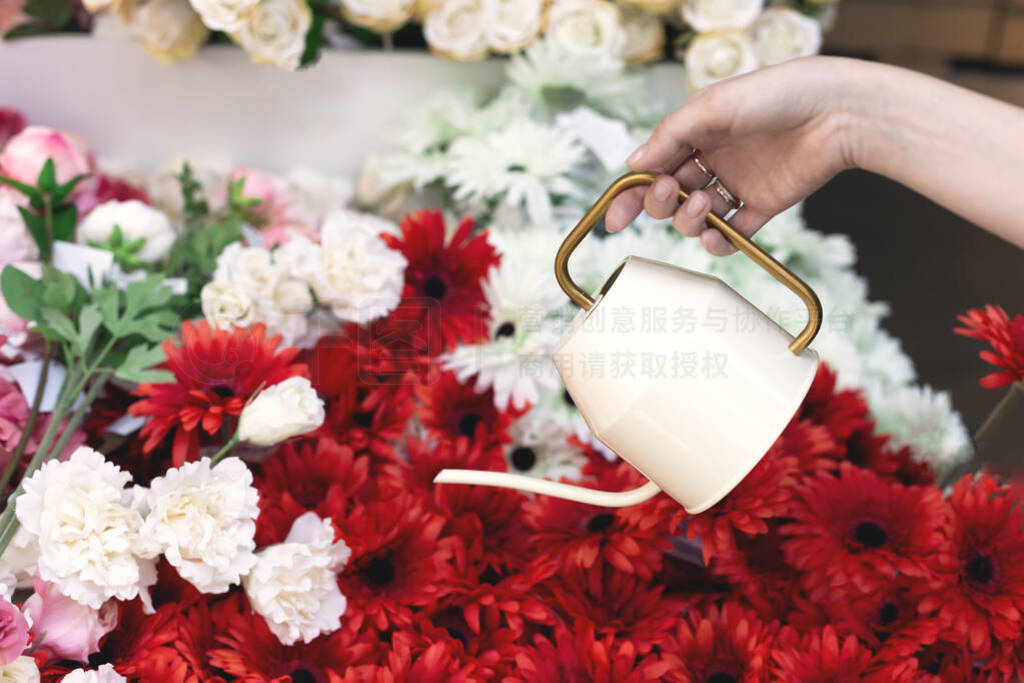 Elegant watering can in female hands with colorful flowers on th