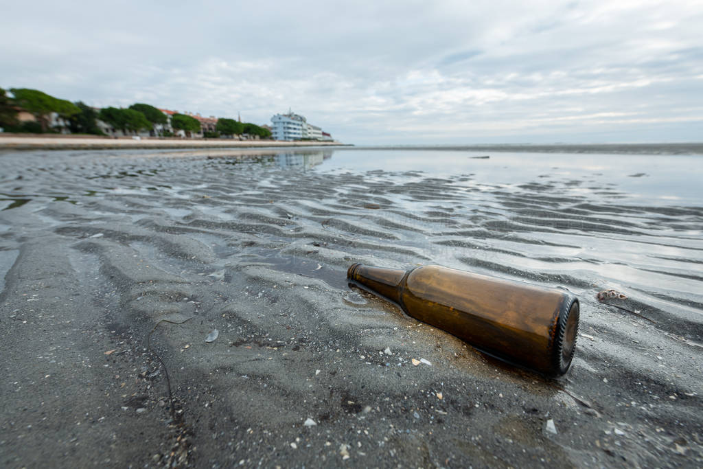 Empty bottle lying on the beach of Grado on a cloudy day in late