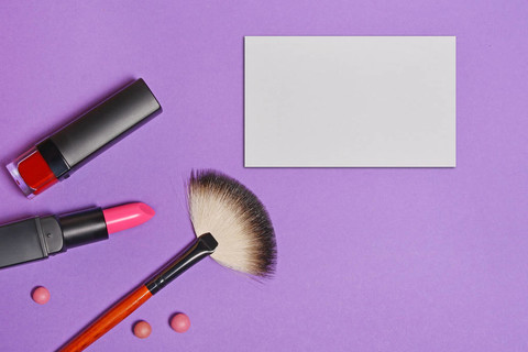 美容产品套装的顶视图: 装饰化妆品如唇膏、指甲油、化妆刷和明亮紫色背景上的模拟名片