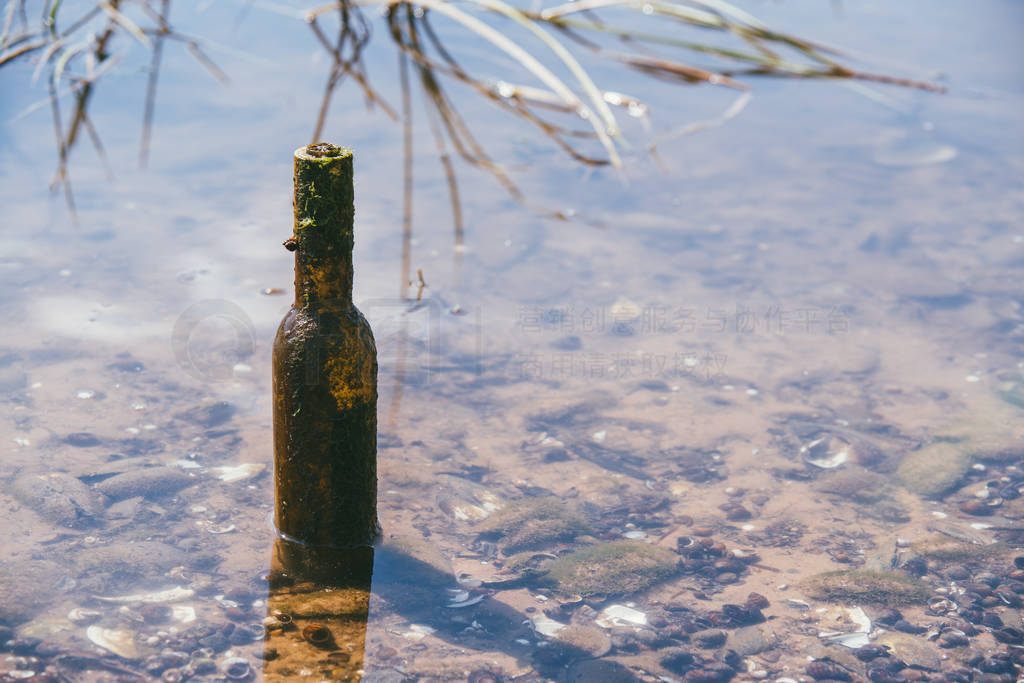 Empty dirty glass bottle in the clear water of the river. Concep