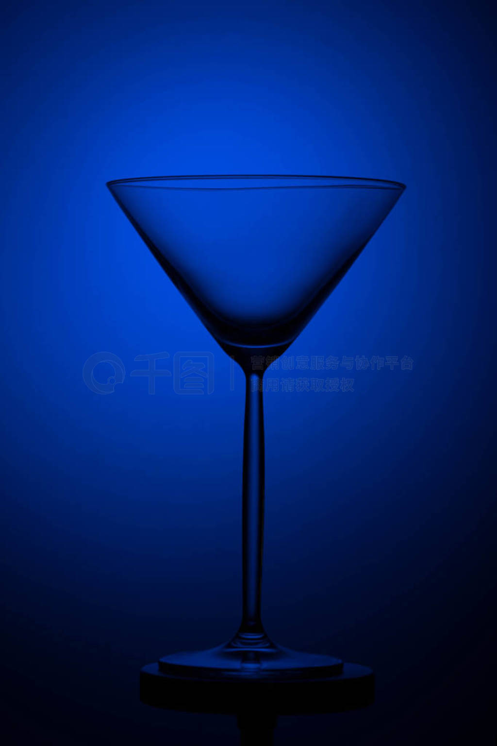 Empty tall martini glass on a black and blue background