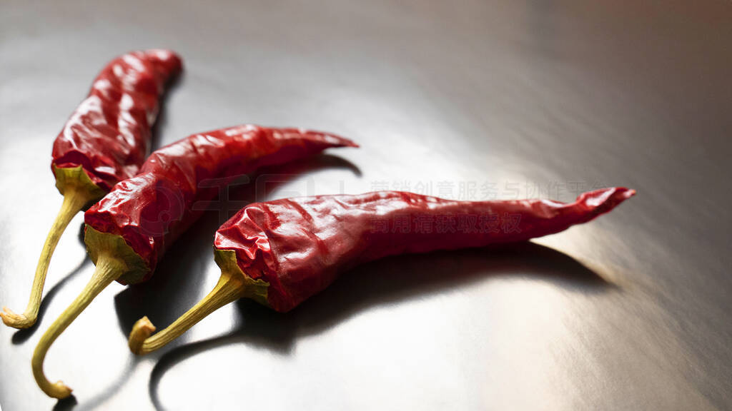 Three dried red chilli on a grey background