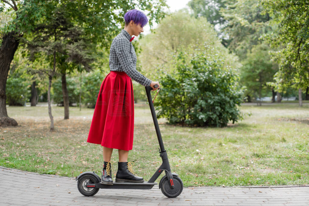 A young woman with purple hair rides an electric scooter in a pa