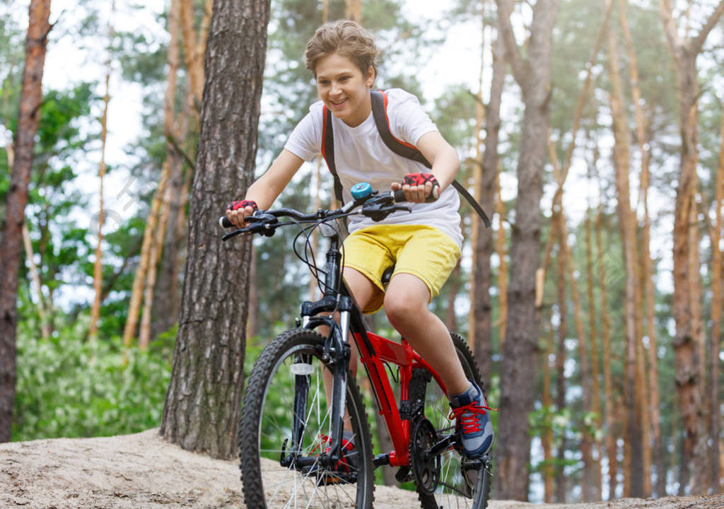 儿童少年穿白色t恤和黄色短裤骑自行车在森林在春天或夏天快乐的微笑