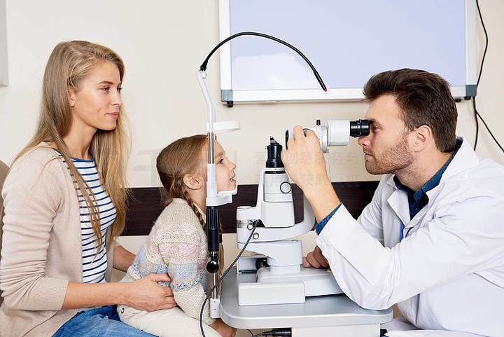 年轻验光师的侧面图在眼科门诊检查中使用狭缝灯检测小女孩的视力
