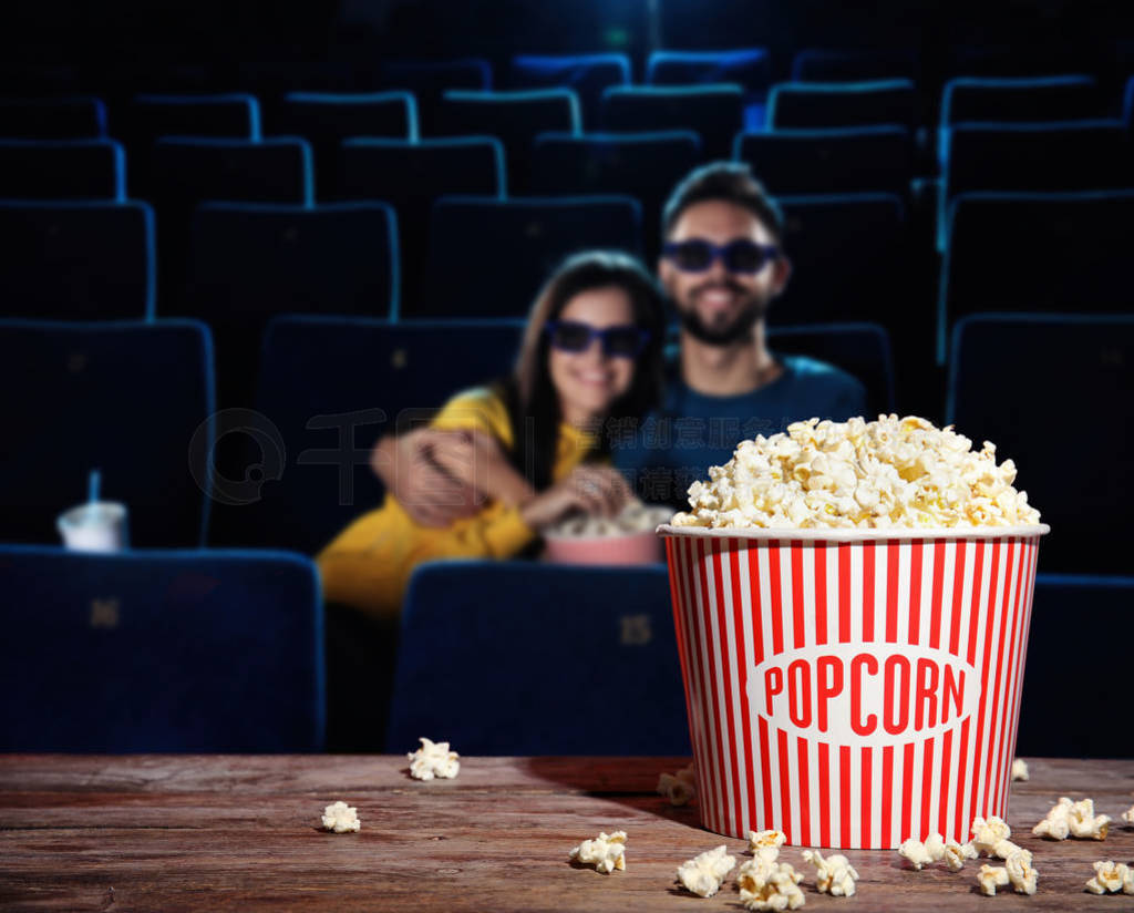 Bucket of popcorn on wooden table in cinema hall. Space for text