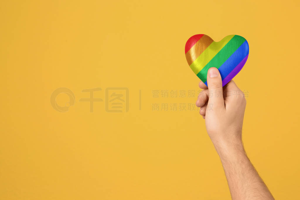 Man holding rainbow heart on color background, closeup with spac