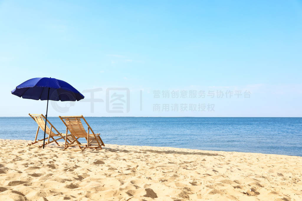 Empty wooden sunbeds and umbrella on sandy shore. Beach accessor