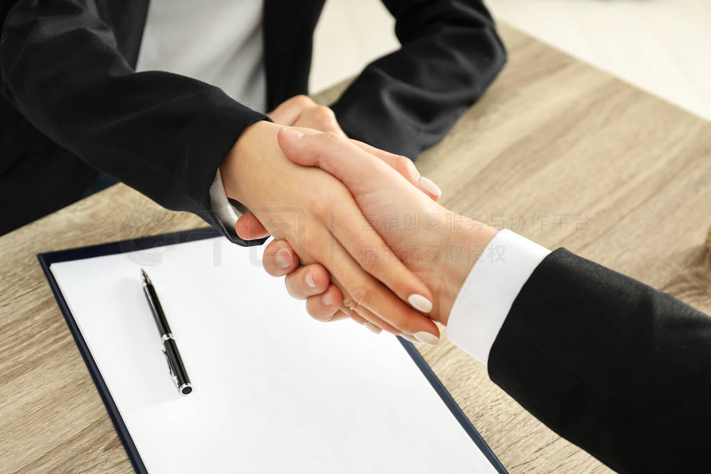 Real estate agent shaking hands with client at table in office,