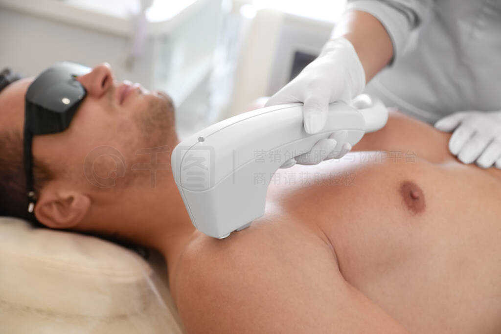 Young man undergoing laser epilation procedure in beauty salon,