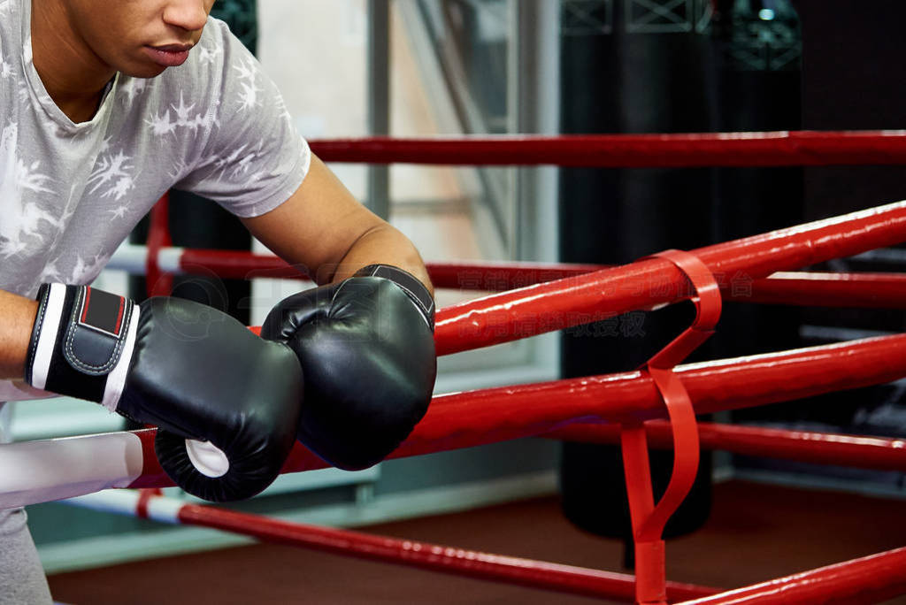 Professional young boxer resting on the ropes of the ring after