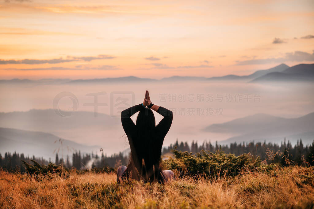 woman sits on top of a mountain at sun rise.
