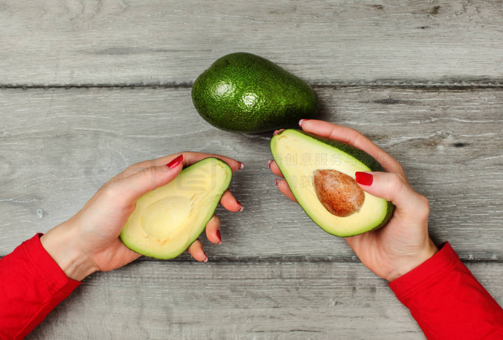 Tabletop view, woman hand holding two halves of avocado in each