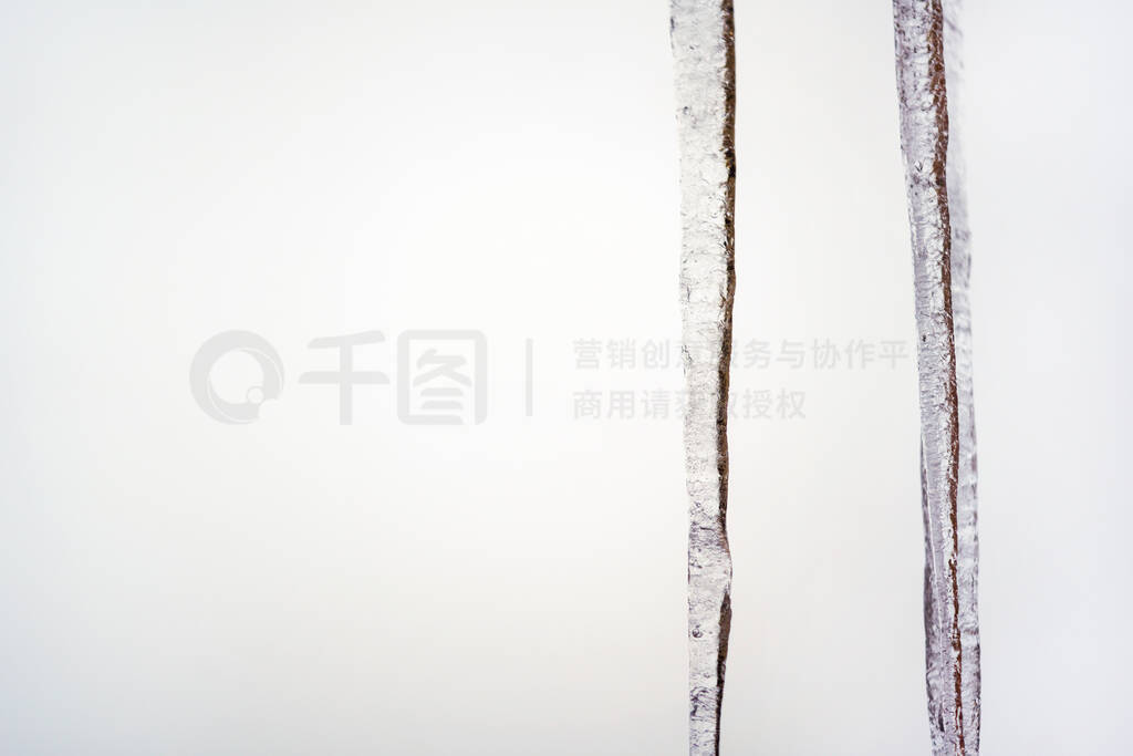 Two icicles hanging from roof, white overcast background, space