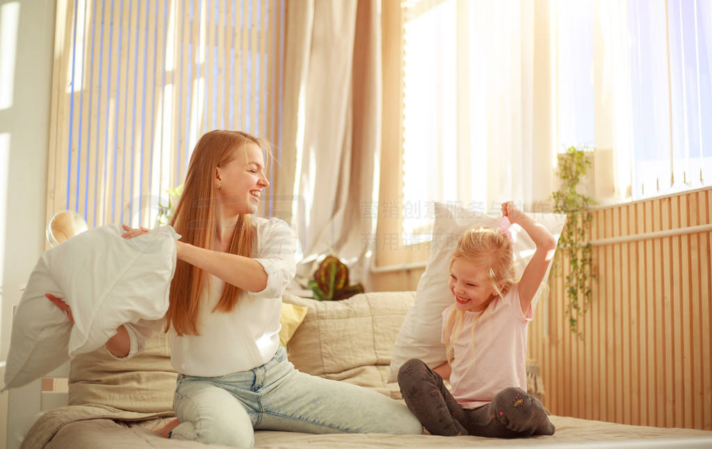 Mother and daughter joyfully play together with pillows at home