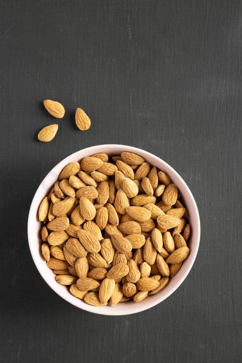 Full pink bowl of almonds over black background, overhead view.