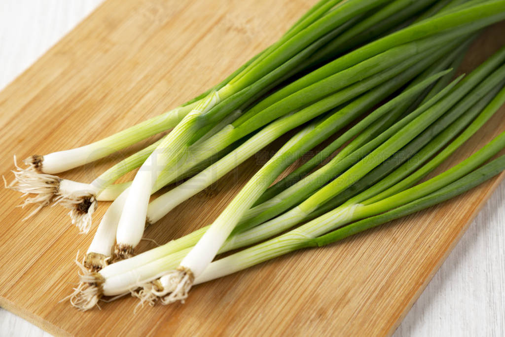 Fresh green onions on a bamboo board on a white wooden surface,