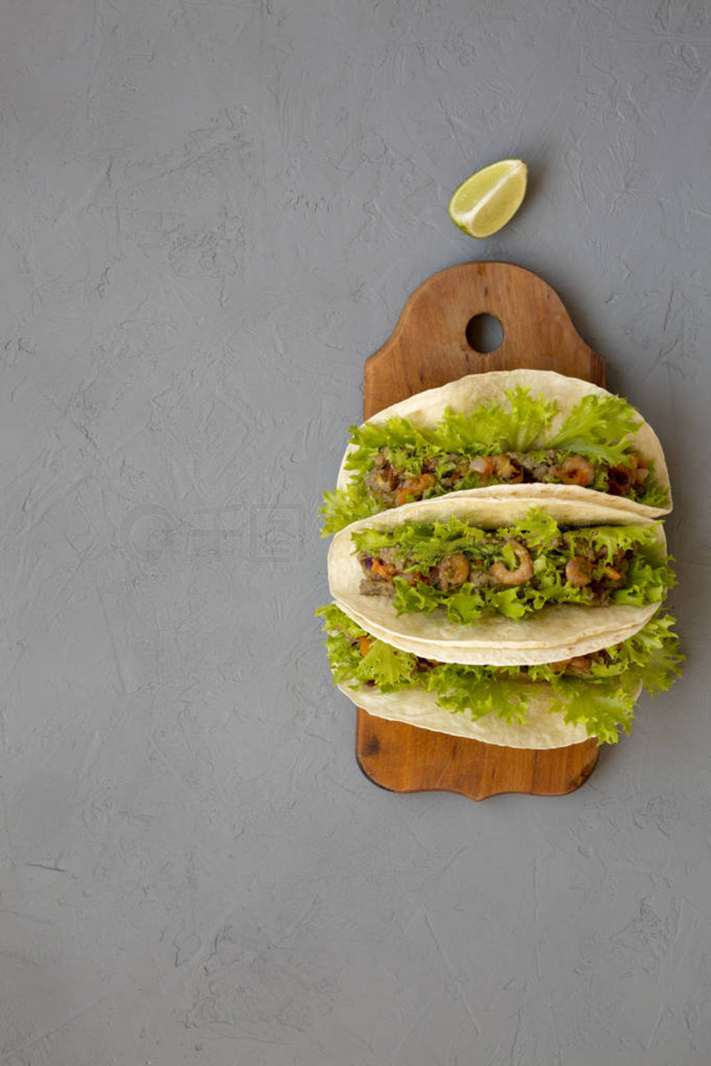 Shrimp tacos on a rustic wooden board on a gray background, top