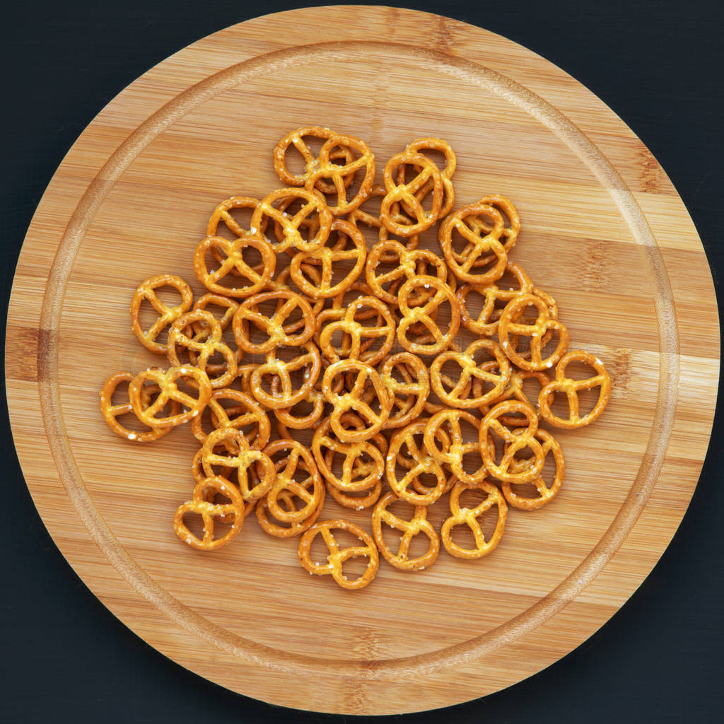 Salt pretzels on a round bamboo board on a dark background, top