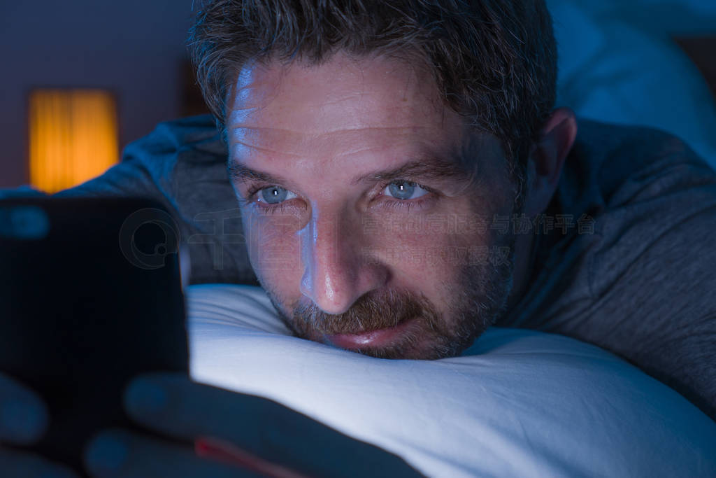 happy man with blue eyes lying on bed late at night in dark ligh